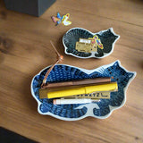 Two ceramic leaf-shaped bowls on a wooden surface with stationery items inside.