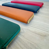 Four colorful pen cases (green, orange, blue, red) on a light wooden surface.